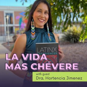 Dra. Hortencia Jimenez stands outside, holding a copy of the book titled Latinx Experiences. She wears colorful, intricate beadwork earrings and a matching bracelet that reflect Indigenous designs, along with a teal sleeveless top. Her long dark hair flows over her shoulders as she smiles warmly at the camera. The background features a building with vibrant murals and lush greenery. The podcast title La Vida Más Chévere is prominently displayed in large pink letters at the bottom, along with the subtitle with guest Dra. Hortencia Jimenez on a light green banner.